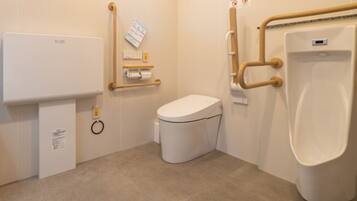 A small, modern bathroom with a toilet, urinal, and a handrail for accessibility.