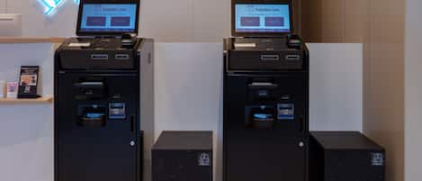 Two self-service kiosks with screens, a neon sign, and a small shelf with brochures.