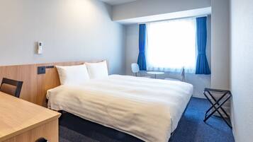 Quarto de hotel com cama, escrivaninha, cadeira, mesinha e janela com cortinas.
