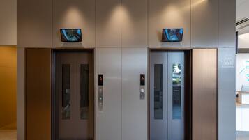 Duas portas de elevador com painéis digitais acima, em um interior de edifício moderno.