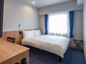 Quarto de hotel com uma cama, uma escrivaninha e uma cadeira.