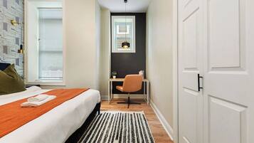 A hotel room with a bed, a desk, a chair, a window, and a door.