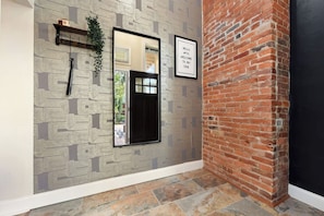 A hallway with patterned wallpaper, a black-framed mirror, a welcome sign, and a brick wall. - Netflix+BBQ+Free Parking Near Shops in East Liberty (Pittsburgh)