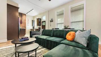 A living room with a sectional sofa, a coffee table, and a kitchen in the background.