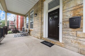 Un bâtiment en pierre avec une porte brun foncé, une boîte aux lettres et un porche couvert avec des chaises.