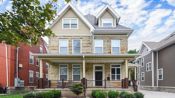 A two-story residential building with a front porch, stone facade, and a clear sky.