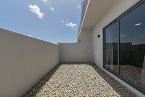 A balcony with a gravel floor, a glass door, and a clear sky. - Sleek 2BR Retreat, Tanki Leendert (Tanki Leendert)
