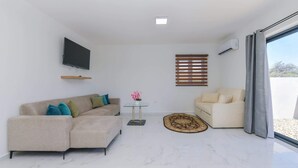 Ein modernes Wohnzimmer mit einer Couch, einem Couchtisch, einem an der Wand montierten Fernseher und einem Fenster mit Jalousien.