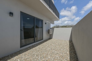 A modern building with a large sliding glass door, a small air conditioning unit, and a gravel ground. - Sleek 2BR Retreat, Tanki Leendert (Tanki Leendert)