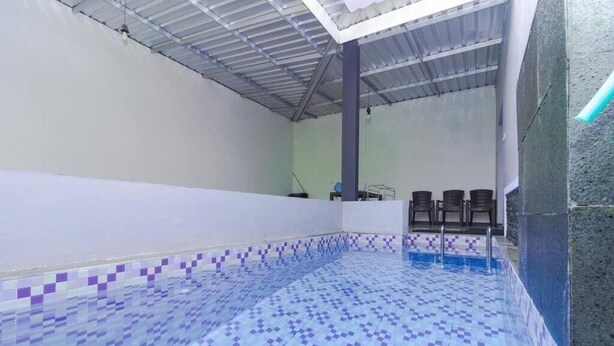 Una piscina con suelo y paredes de baldosas, techo con vigas metálicas y algunas sillas cerca de la piscina.