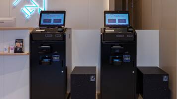 Dos quioscos de autoservicio con pantallas mostrando la página web de 'toyako inn', ubicados en un moderno vestíbulo de hotel con un letrero de neón al fondo.