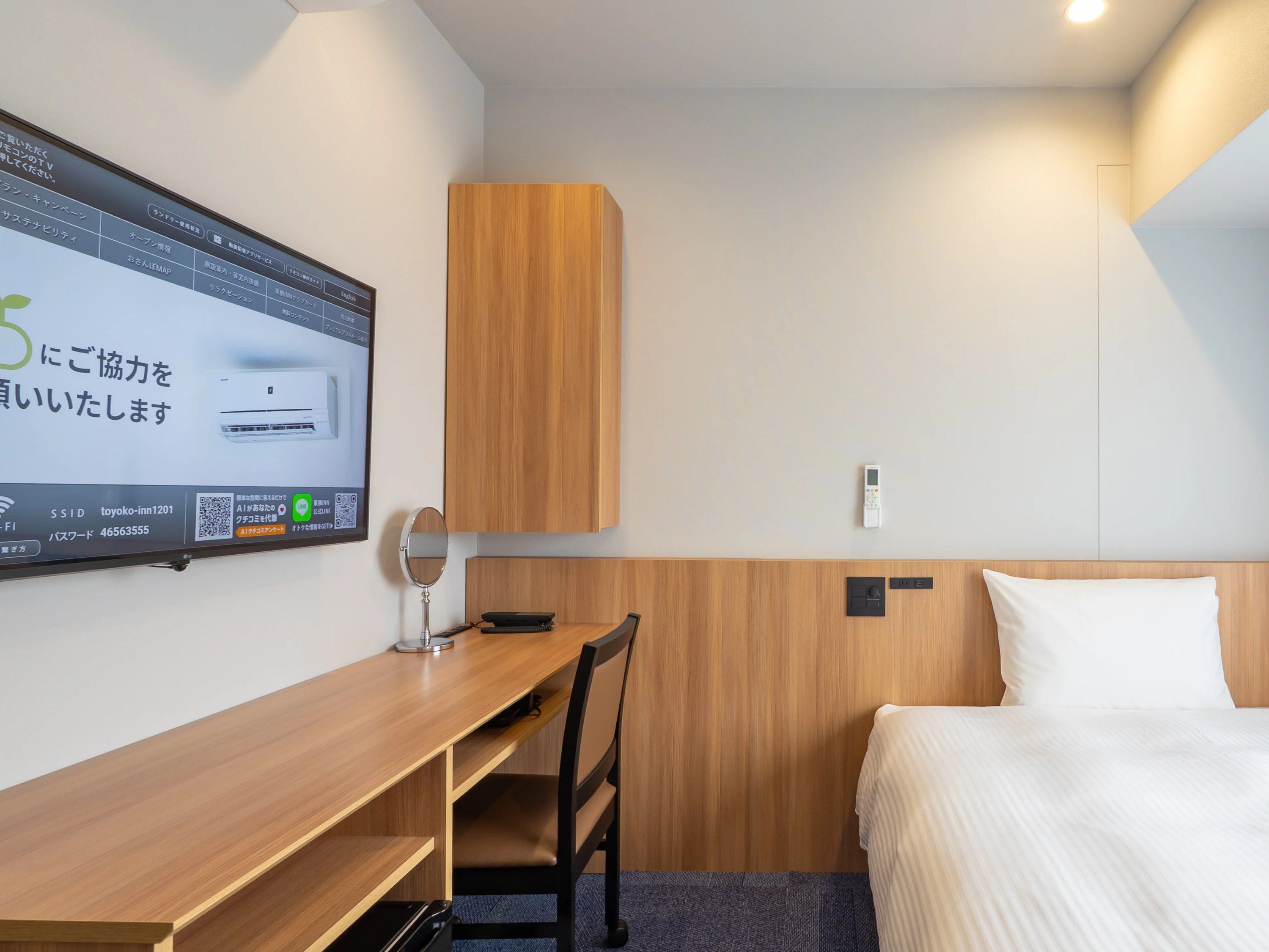 Ein Hotelzimmer mit einem Bett, einem Schreibtisch, einem Stuhl, einem Wandspiegel und einem Thermostat.