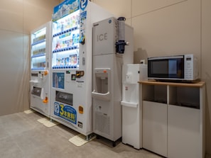Máquina expendedora con dispensador de agua y un microondas sobre un estante de madera.