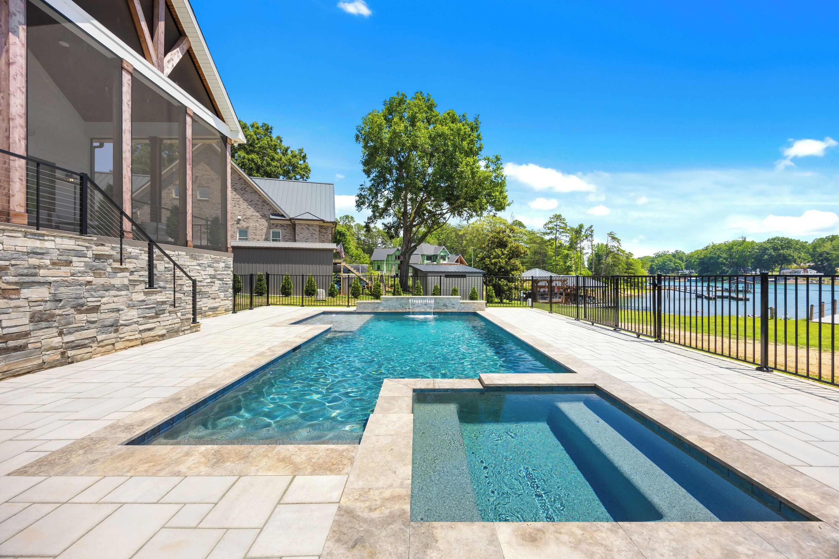 Una piscina con un deck de piedra y vista a un lago.
