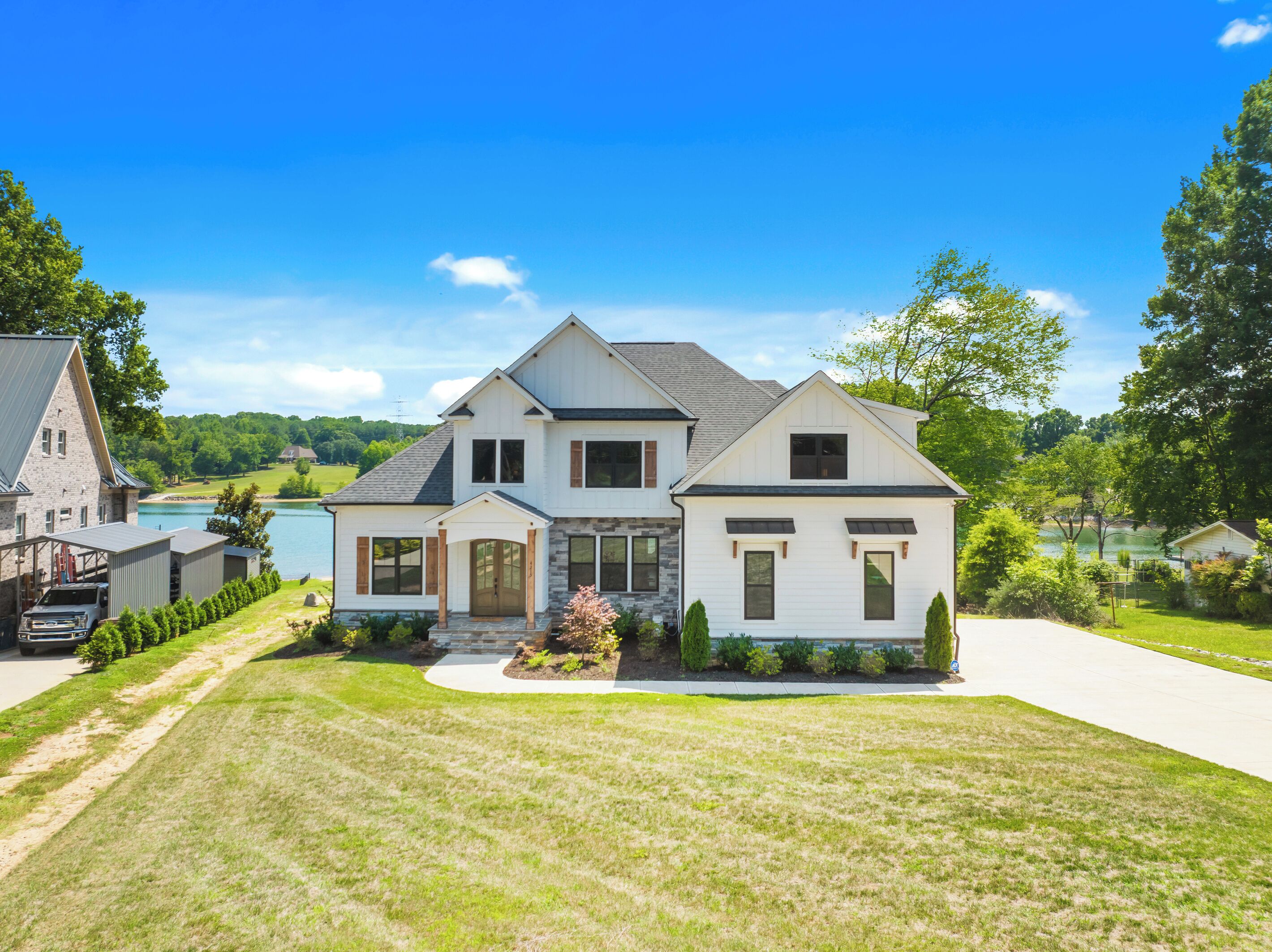 A two-story house with a stone facade, a large front porch, and a view of a lake.