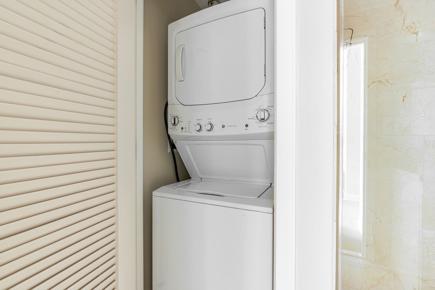 A front-loading washer and dryer unit with a control panel, installed in a laundry room with a sliding door.