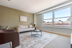 Ein Wohnzimmer mit Sofa, Couchtisch und einem großen Fenster mit Blick auf Gebäude.