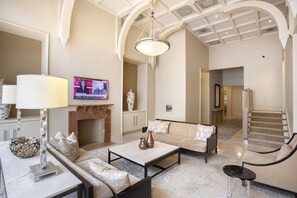 Ein geräumiges Wohnzimmer mit Kamin, bequemen Sitzgelegenheiten und einem Fernseher, der eine Nachrichtensendung zeigt.