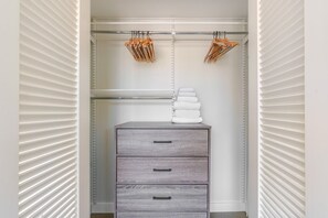 A walk-in closet with a grey storage unit, a metal rod for hanging clothes, and a stack of white towels. - Blueground | Penn Quarter, pool, nr National Gallery (Washington, D.C.)
