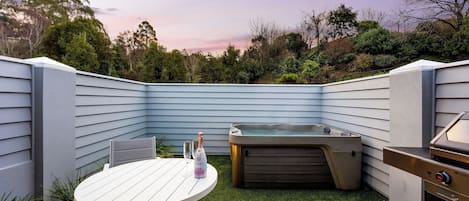 A backyard with a white table, a hot tub, and a grill.