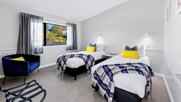 Ett hotellrum med två sängar, en blå stol, ett litet bord och utsikt över omgivningarna.