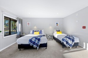 A hotel room with two beds, a window with curtains, a small table, and a wall-mounted light. - Myhub Holiday Park (Dunedin)