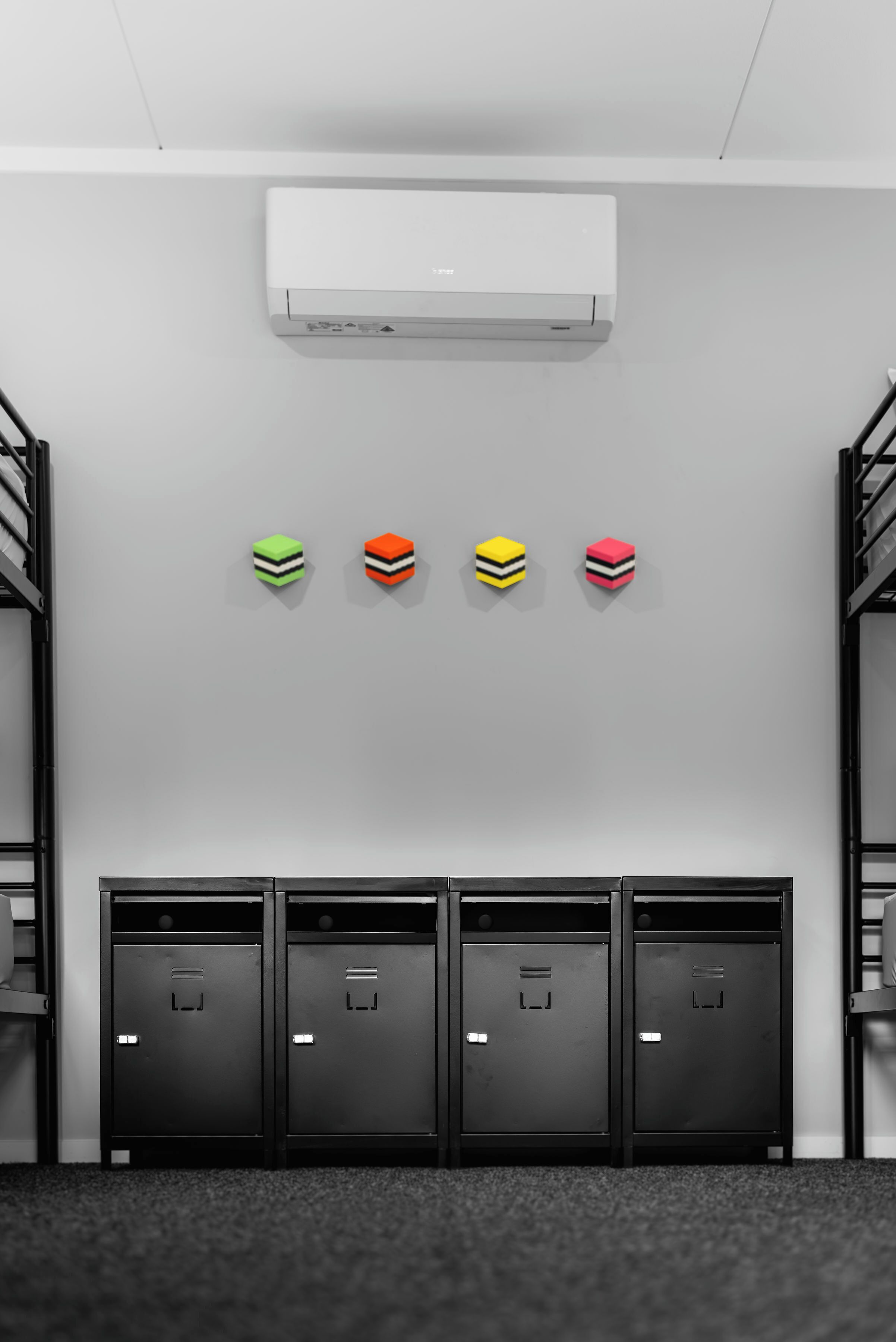 Una habitació amb lliteres, aire condicionat fixat a la paret i quatre armaris amb decoracions de cubs de colors.