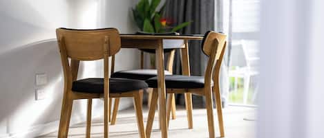 A dining area with a wooden table and chairs, carpeted floor, and a plant in the background.