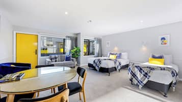 Quarto de hotel moderno com área de jantar, duas camas com decoração harmoniosa, uma janela grande e vista para o exterior.