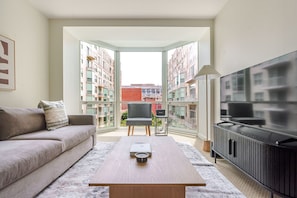 A modern living room with a sofa, a coffee table, a TV, and a view of a cityscape through large windows. - Blueground | Penn Quarter, pool, nr National Gallery (Washington, D.C.)