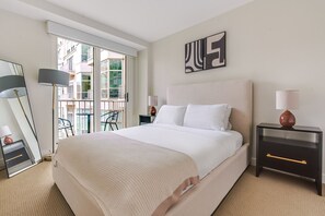 A hotel room with a large bed, a nightstand with a lamp, a chair, a mirror, and a view of the outside balcony. - Blueground | Penn Quarter, pool, nr National Gallery (Washington, D.C.)