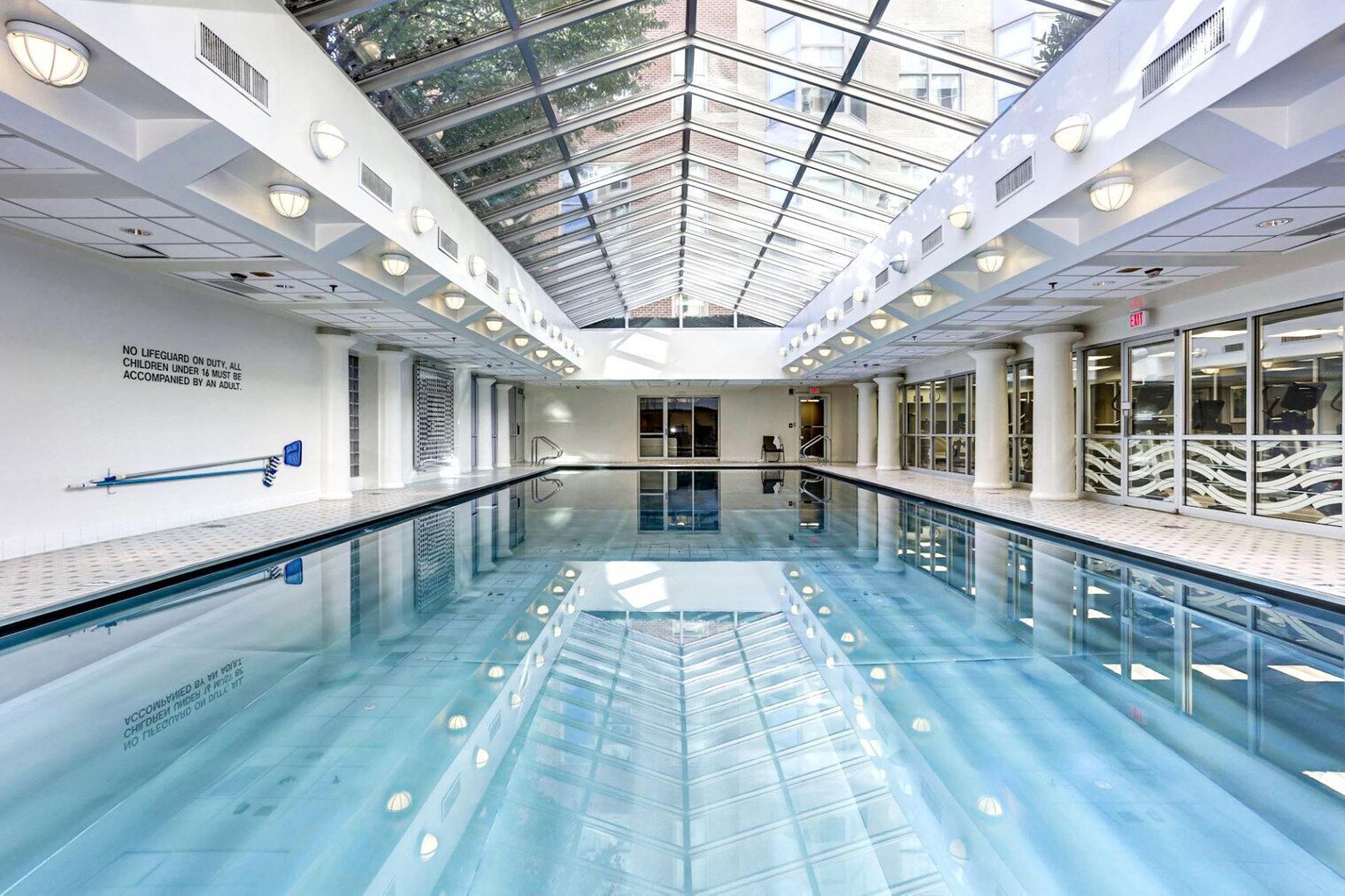 A modern indoor swimming pool with a glass ceiling, clear water, and a lifeguard station.