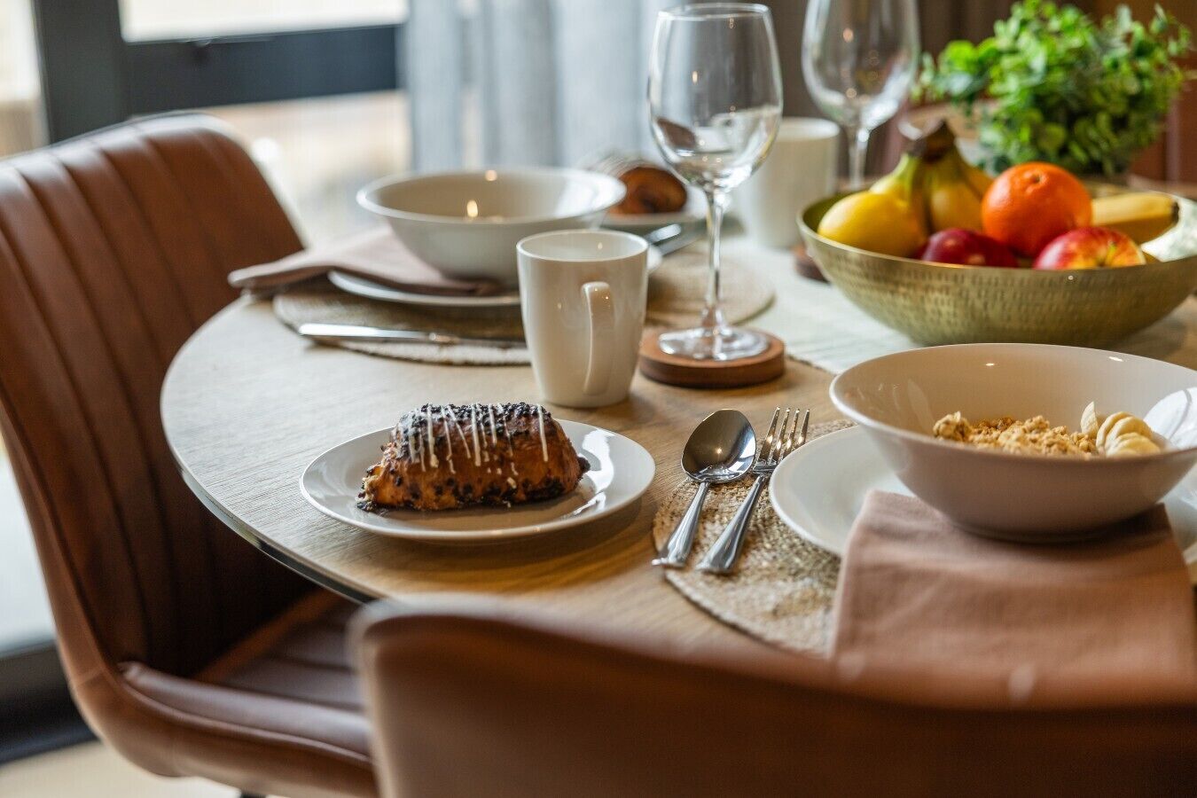 A dining table with a dessert, fruit bowl, and breakfast items.