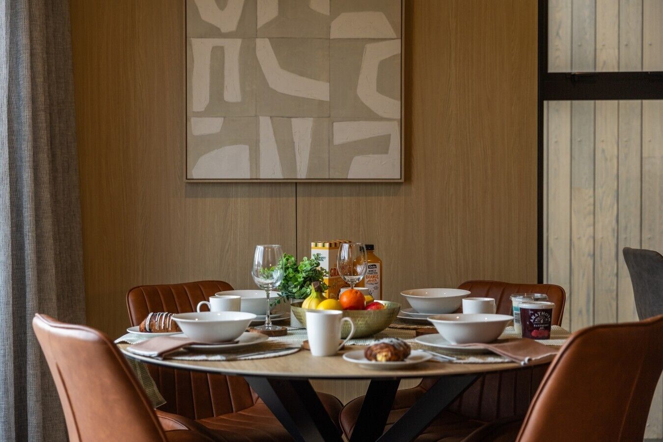 A dining table set with white plates, bowls, and cups, surrounded by brown chairs.