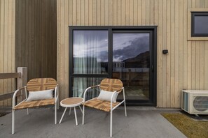 A modern outdoor seating area with two chairs and a small table, a sliding glass door, and an air conditioning unit.