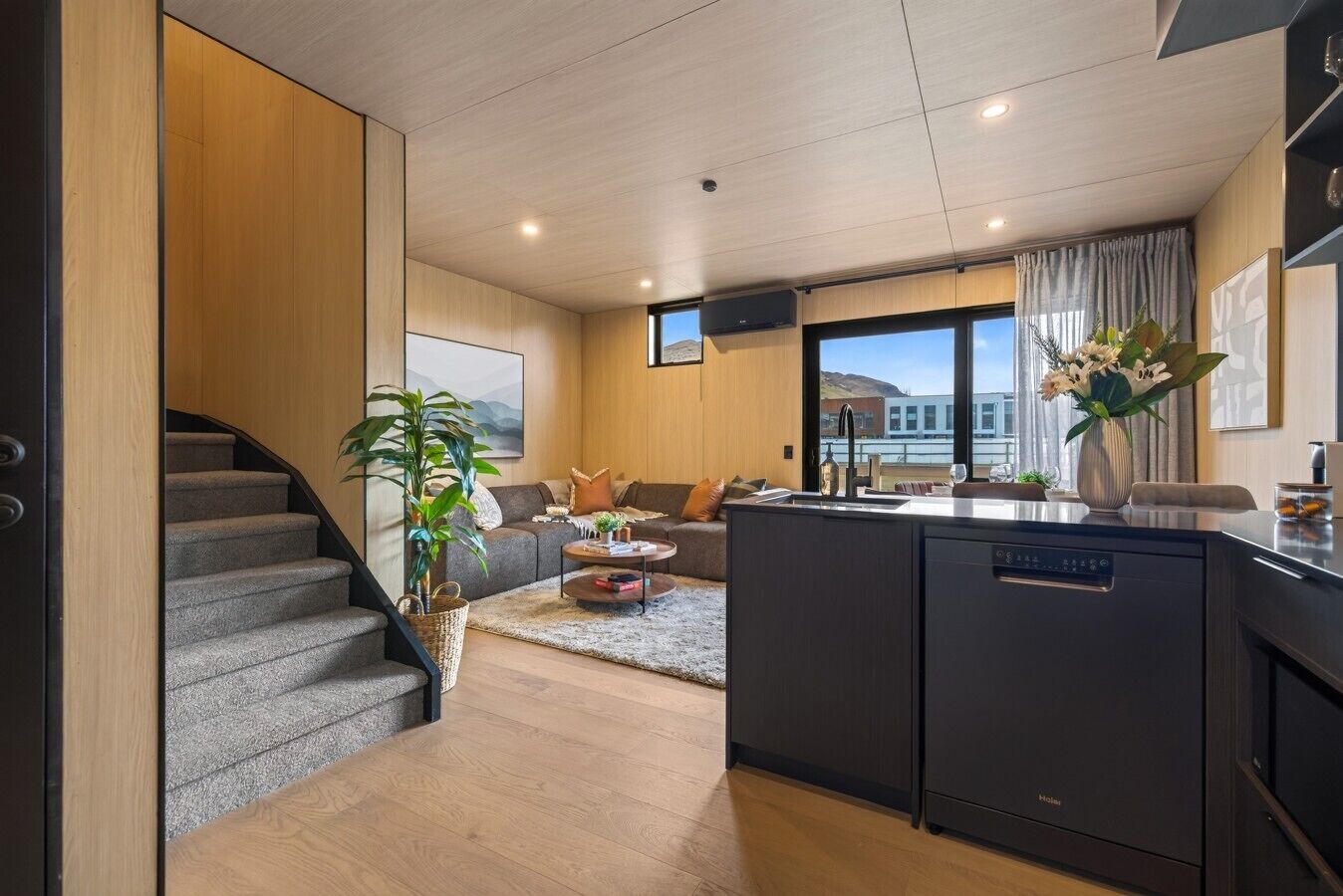A modern living room with a sofa, coffee table, and a view of a building through large windows.