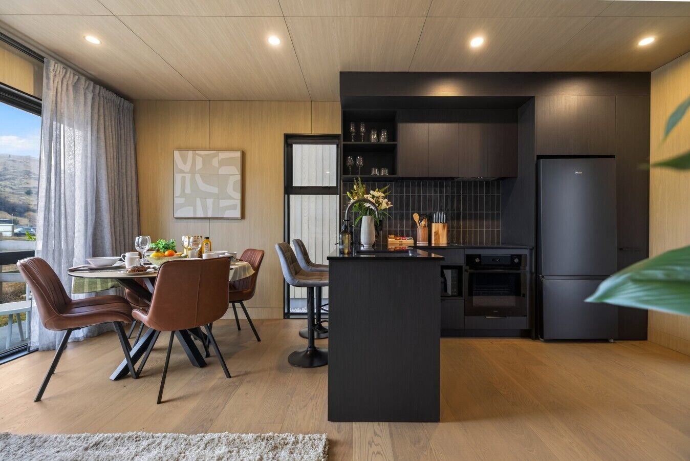 Una cocina moderna con una isla central, suelo de madera y un comedor con sillas y una mesa.