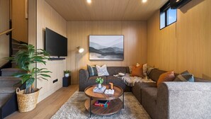 Un soggiorno moderno con un divano, un tavolino, una TV a schermo piatto, un quadro e una scala.