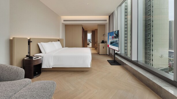 Habitación de hotel moderna con una cama grande, televisión, zona de estar y vistas a la ciudad.