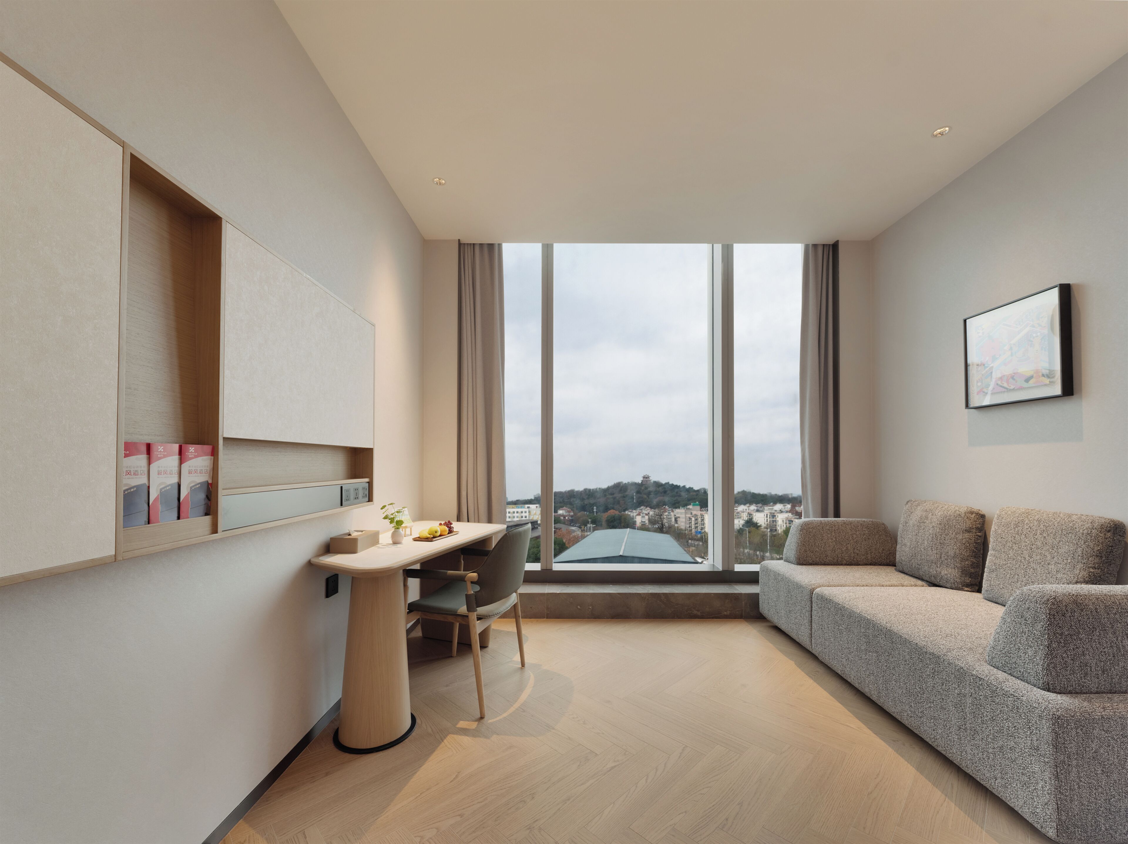 Habitació d'hotel moderna amb una finestra gran, un sofà, un escriptori amb una cadira i una taula petita.
