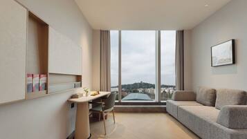 Habitació d'hotel moderna amb una finestra gran, un sofà, un escriptori amb una cadira i una taula petita.