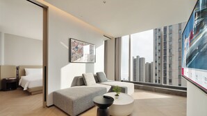 Una habitación de hotel moderna con cama, sofá, mesa de centro y un ventanal con vista a la ciudad.