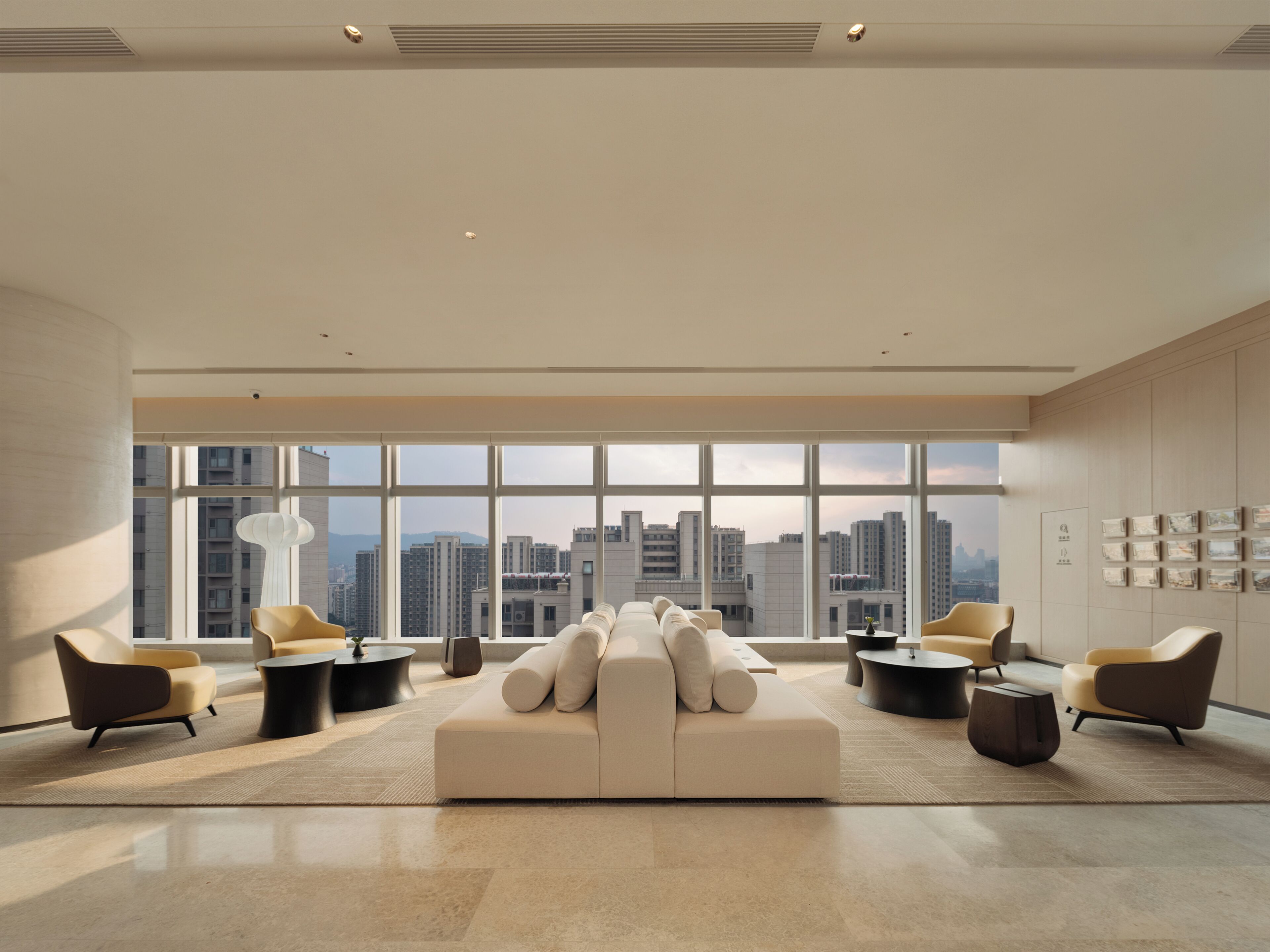 A modern living room with a large sofa, armchairs, and a city view through expansive windows.