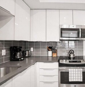 A modern kitchen with stainless steel appliances, a coffee maker, and a kettle on the counter. - 18th Floor|High Rise Studio|King Bed + Parking! (Charlotte)