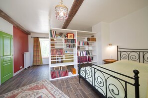 Ein Schlafzimmer mit einem Bett, einem weißen Bücherregal, einem Heizkörper, einer grünen Tür und einem Fenster mit Vorhängen.