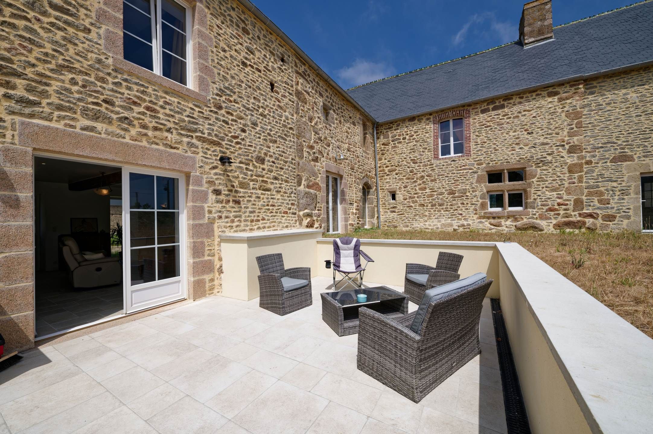 A stone building with a patio area featuring wicker furniture and a glass table.