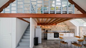 A loft-style kitchen with a stone wall, a dining area with a table and chairs, and a staircase leading to a second floor.