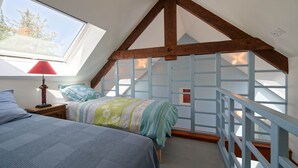 A bedroom with a sloped ceiling, a bed with a floral bedspread, a nightstand with a lamp, and a window with a view of trees.