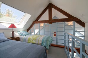 A bedroom with a sloped ceiling, a bed with a floral bedspread, a nightstand with a lamp, and a window with a view of trees.