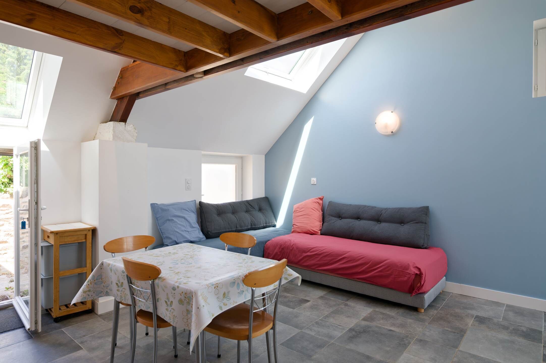 Una habitación acogedora con una mesa de comedor, sillas, un sofá con cojines y un tragaluz.